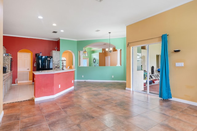 kitchen featuring black refrigerator, crown molding, decorative light fixtures, a center island with sink, and a chandelier