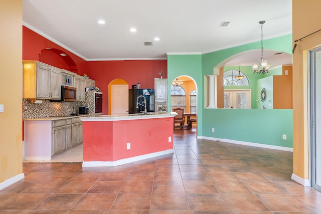 kitchen with black refrigerator, decorative backsplash, tile patterned floors, a center island with sink, and a chandelier