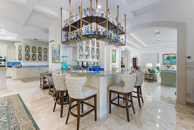 kitchen with cream cabinetry, dark stone counters, a kitchen bar, decorative backsplash, and beam ceiling