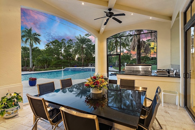 pool at dusk featuring ceiling fan, a patio, pool water feature, and exterior kitchen