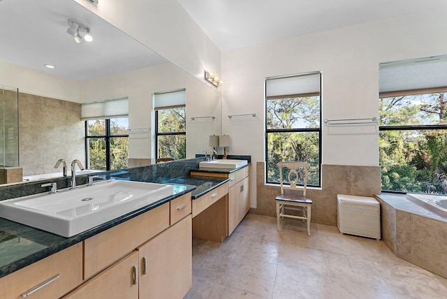 bathroom featuring plenty of natural light, tile patterned flooring, a relaxing tiled tub, and vanity