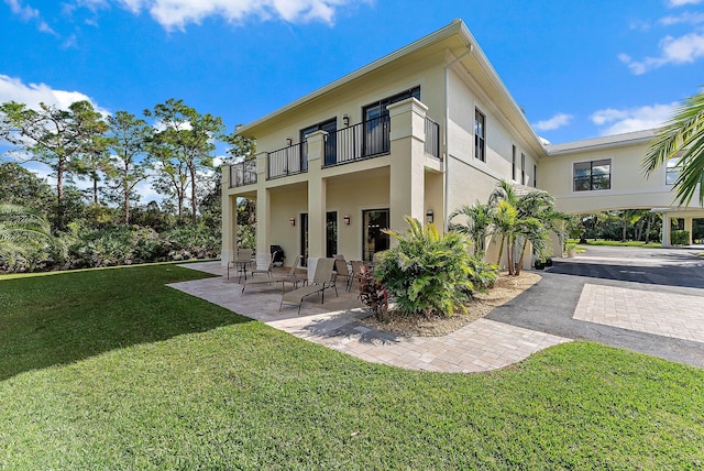 rear view of house with a lawn, a balcony, and a patio