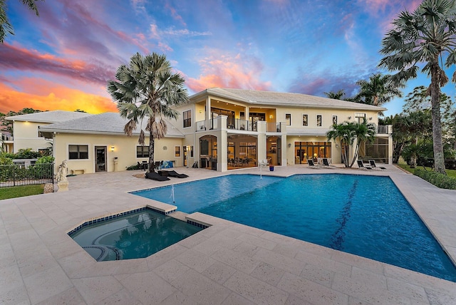 pool at dusk featuring a patio area and an in ground hot tub