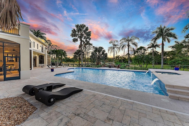 pool at dusk with pool water feature, a patio area, and an in ground hot tub