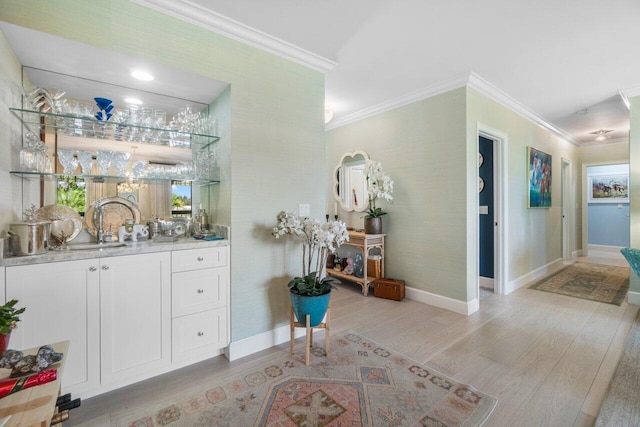 bar featuring crown molding, sink, light wood-type flooring, and white cabinets