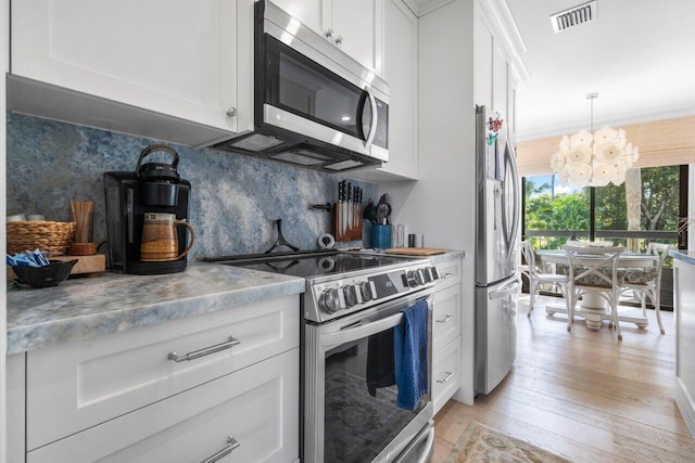 kitchen with appliances with stainless steel finishes, white cabinetry, backsplash, decorative light fixtures, and light wood-type flooring