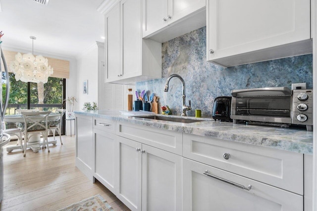 kitchen with sink, white cabinetry, hanging light fixtures, light stone countertops, and decorative backsplash