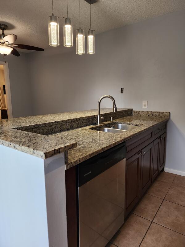 kitchen with pendant lighting, dishwasher, sink, a textured ceiling, and light stone counters