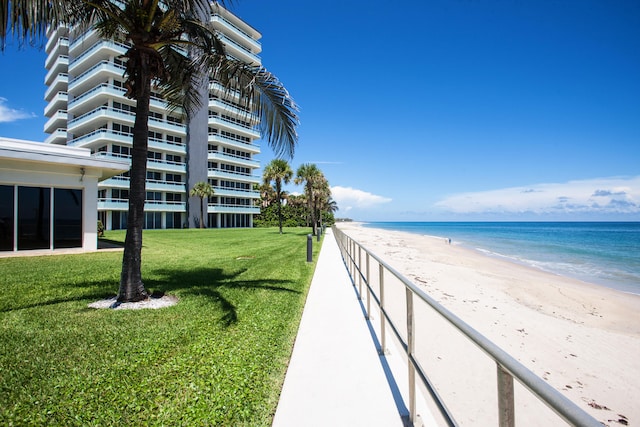 view of community with a yard, a water view, and a beach view