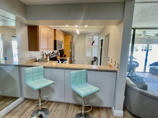 kitchen with decorative backsplash, appliances with stainless steel finishes, kitchen peninsula, ceiling fan, and light hardwood / wood-style flooring