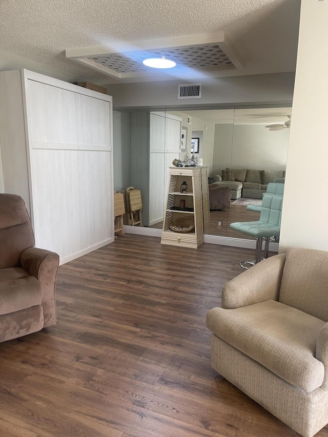 living area featuring ceiling fan, dark wood-type flooring, and a textured ceiling