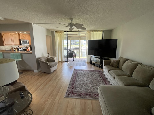 living room with ceiling fan, light hardwood / wood-style flooring, and a textured ceiling