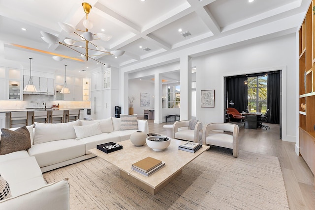 living room featuring beam ceiling, light hardwood / wood-style floors, a notable chandelier, and coffered ceiling