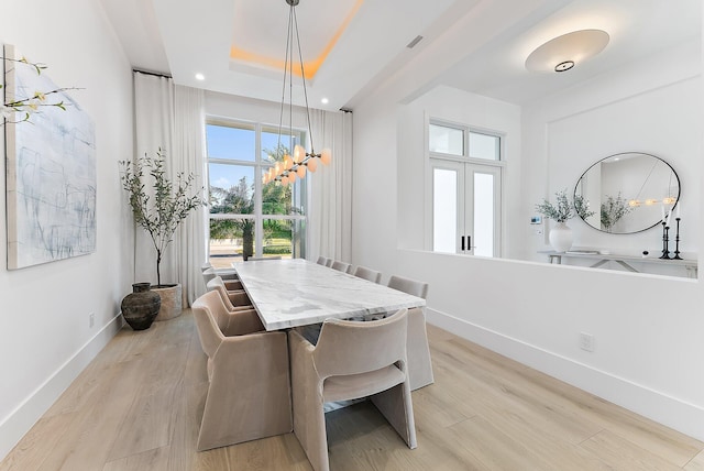 dining area with light hardwood / wood-style floors and a tray ceiling