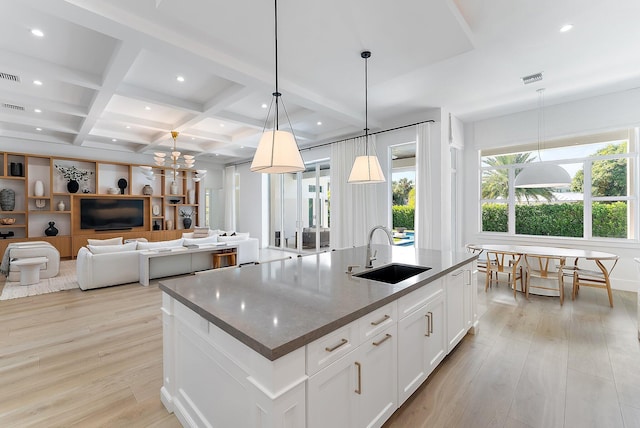 kitchen with coffered ceiling, sink, pendant lighting, a center island with sink, and white cabinets