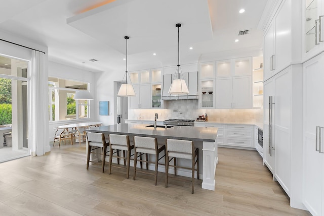 kitchen featuring decorative backsplash, a kitchen island with sink, sink, decorative light fixtures, and white cabinetry