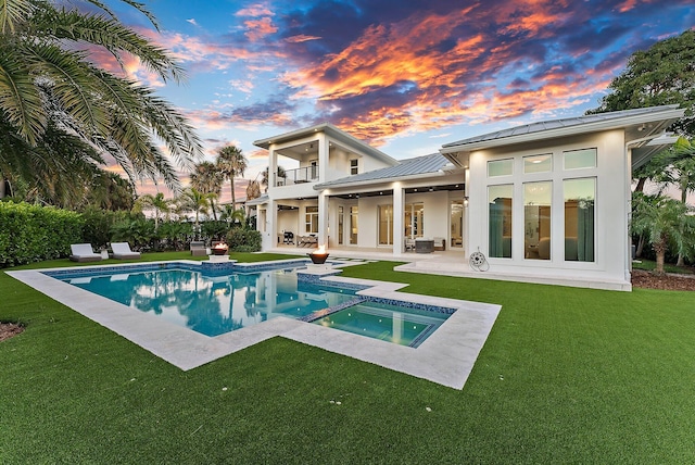 back house at dusk featuring a pool with hot tub, ceiling fan, a balcony, a yard, and a patio