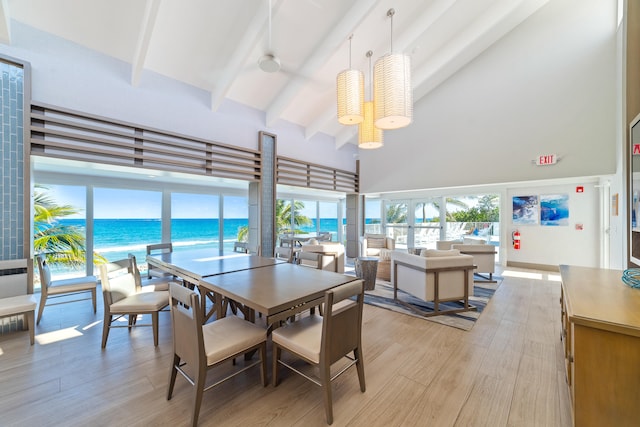 dining space with light hardwood / wood-style floors, a water view, beam ceiling, and high vaulted ceiling