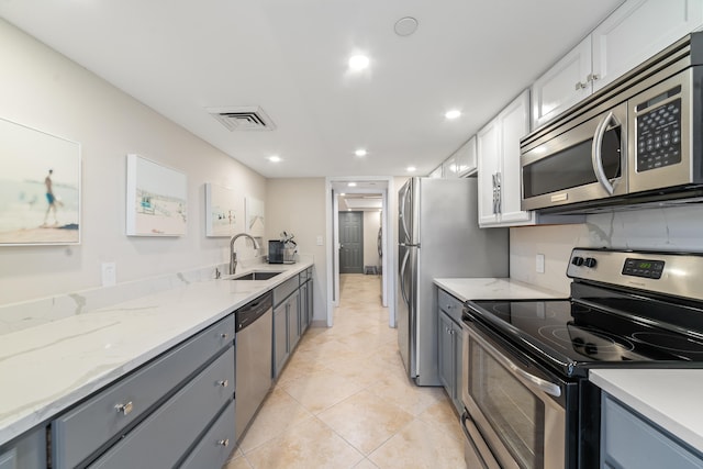 kitchen with sink, light stone counters, light tile patterned flooring, white cabinets, and appliances with stainless steel finishes