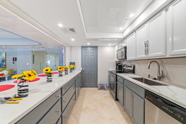 kitchen with light stone countertops, gray cabinetry, stainless steel appliances, sink, and white cabinets