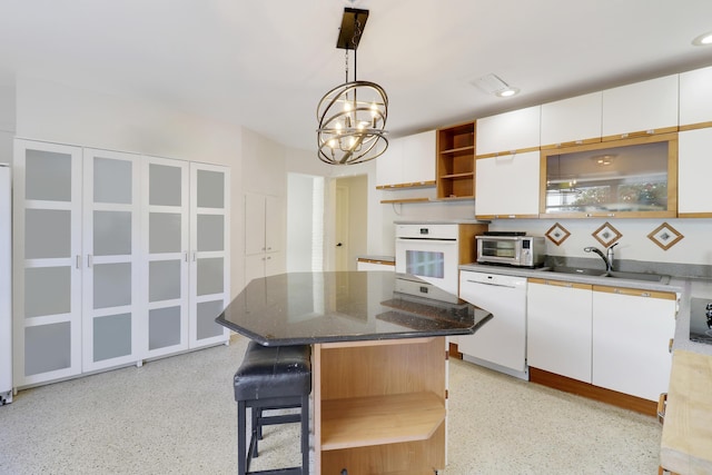 kitchen with pendant lighting, white appliances, white cabinets, sink, and a kitchen island