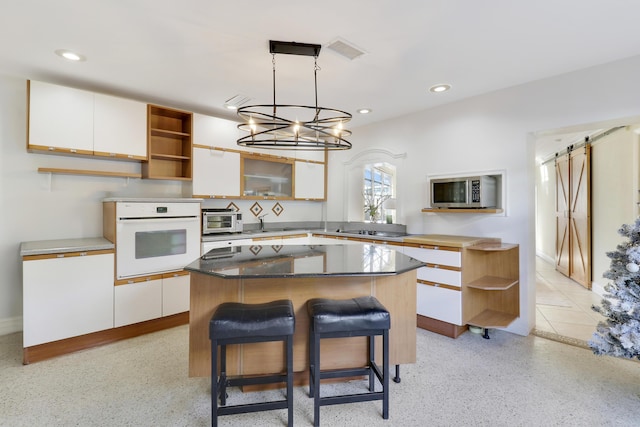 kitchen with a center island, white cabinets, oven, hanging light fixtures, and a barn door