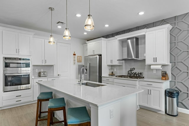 kitchen featuring white cabinetry, wall chimney range hood, stainless steel appliances, and hanging light fixtures