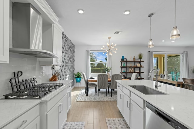 kitchen with tasteful backsplash, wall chimney range hood, pendant lighting, sink, and stainless steel appliances