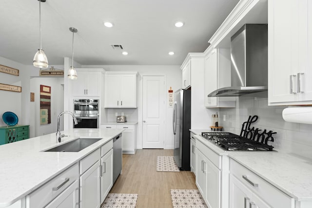 kitchen with wall chimney range hood, decorative light fixtures, sink, and white cabinetry