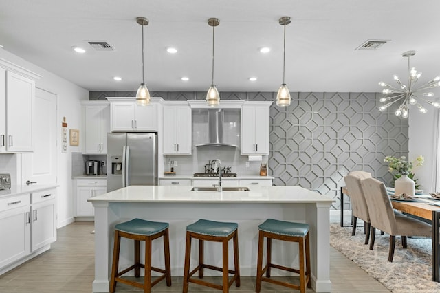 kitchen featuring decorative light fixtures, appliances with stainless steel finishes, a breakfast bar area, white cabinets, and wall chimney exhaust hood