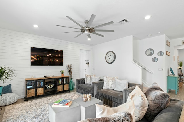 living room featuring ceiling fan, wood-type flooring, and wood walls