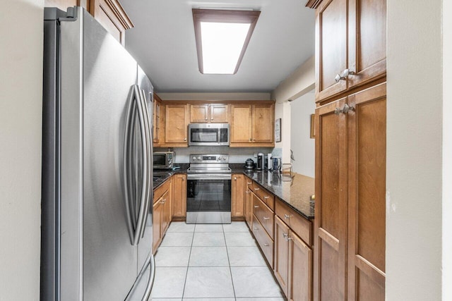 kitchen with light tile patterned floors, stainless steel appliances, and dark stone countertops