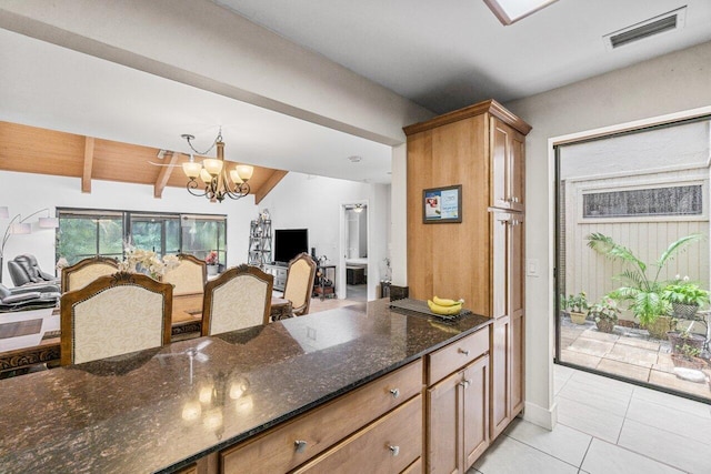 kitchen with hanging light fixtures, vaulted ceiling with beams, dark stone counters, a chandelier, and light tile patterned flooring