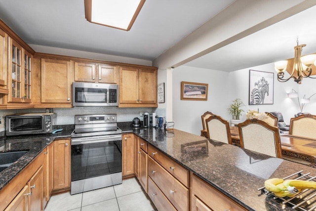 kitchen featuring backsplash, dark stone countertops, a chandelier, light tile patterned flooring, and appliances with stainless steel finishes