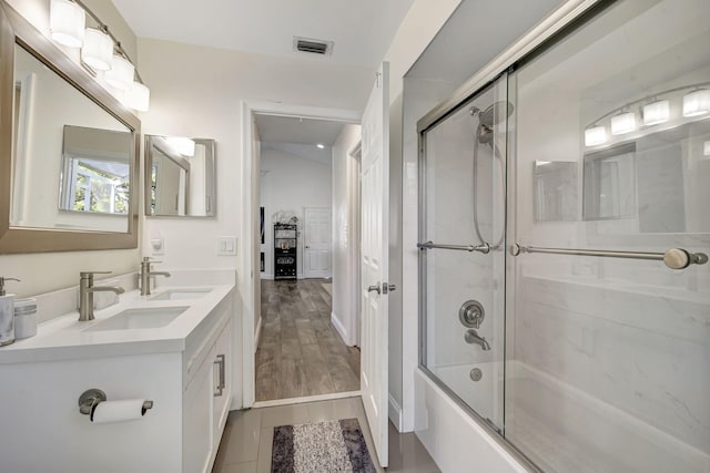 bathroom featuring wood-type flooring, vanity, and bath / shower combo with glass door