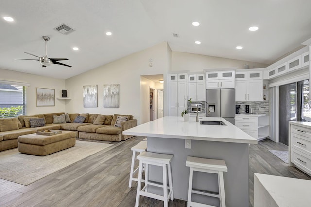 kitchen with a breakfast bar, a center island with sink, stainless steel refrigerator with ice dispenser, decorative backsplash, and white cabinetry