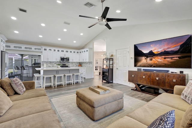 living room with ceiling fan, high vaulted ceiling, and light wood-type flooring