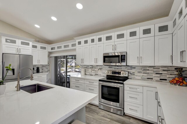 kitchen featuring white cabinetry, sink, tasteful backsplash, lofted ceiling, and appliances with stainless steel finishes