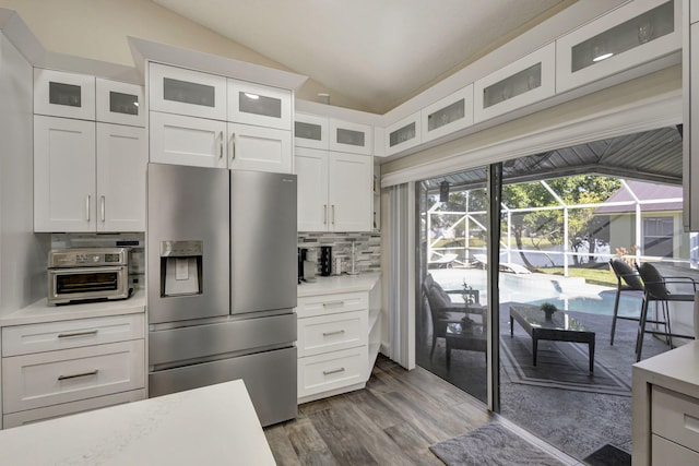 kitchen with stainless steel fridge, backsplash, vaulted ceiling, hardwood / wood-style floors, and white cabinetry