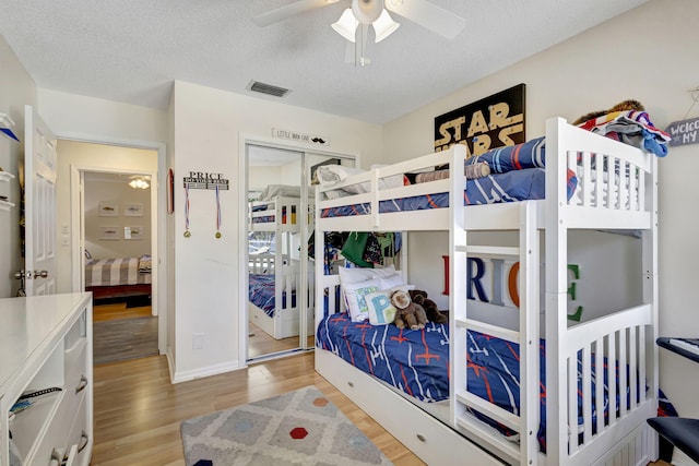 bedroom with a textured ceiling, a closet, light hardwood / wood-style flooring, and ceiling fan