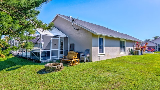 rear view of property with a yard, glass enclosure, central AC unit, and a fire pit