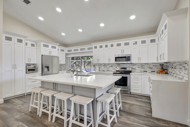 kitchen with a center island with sink, white cabinets, lofted ceiling, and appliances with stainless steel finishes