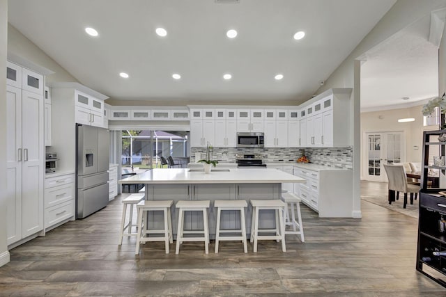 kitchen with white cabinetry, stainless steel appliances, backsplash, an island with sink, and a breakfast bar