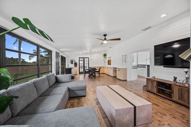 living room featuring ceiling fan, lofted ceiling, wooden walls, and light hardwood / wood-style floors