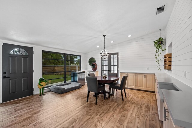 dining room with a chandelier, vaulted ceiling, and light wood-type flooring