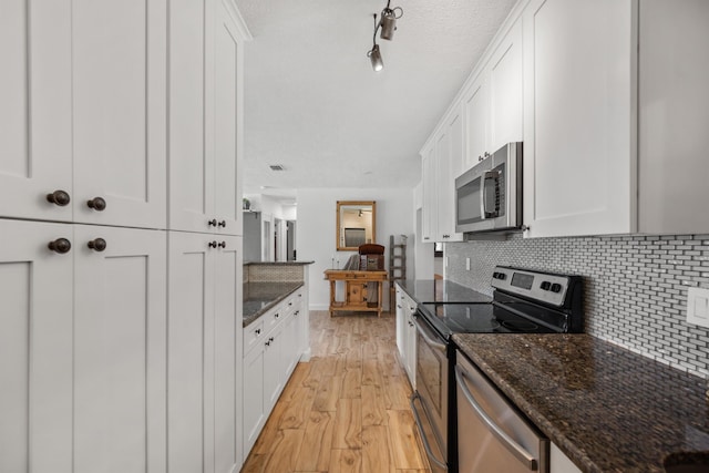 kitchen with white cabinetry, appliances with stainless steel finishes, light hardwood / wood-style flooring, and dark stone counters