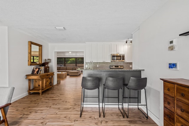 kitchen featuring tasteful backsplash, dark stone countertops, white cabinets, range, and light hardwood / wood-style flooring