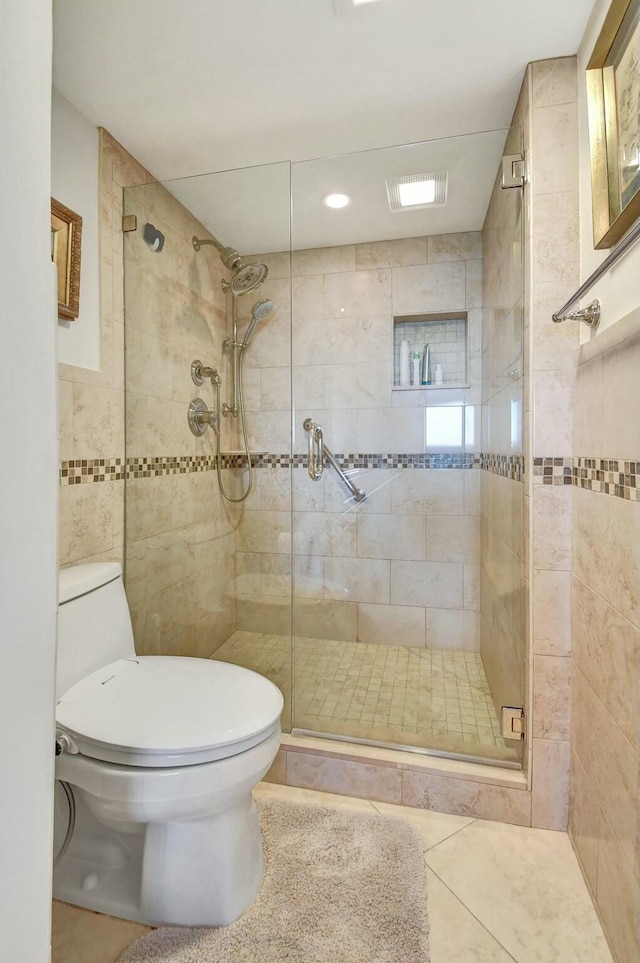 bathroom with tile patterned flooring, toilet, a shower with shower door, and tile walls