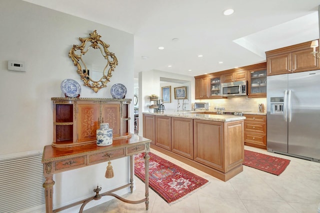 kitchen featuring backsplash, light stone countertops, appliances with stainless steel finishes, light tile patterned flooring, and kitchen peninsula