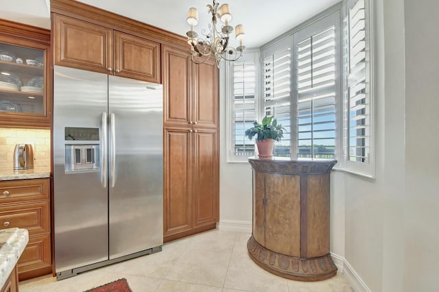 kitchen featuring light stone countertops, stainless steel refrigerator with ice dispenser, a notable chandelier, backsplash, and light tile patterned flooring